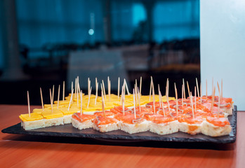 Catering food – canapes with salmon and cheese served on black stone tray on the table. Small sandwiches for banquet or coffee break. Selective focus.