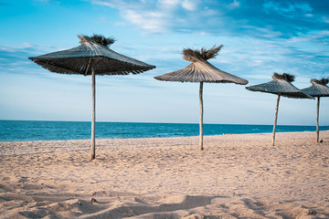 Sandy beach by the sea and wooden sun shelters in the form of umbrellas