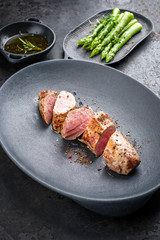 Fried Iberian pork fillet sliced with blanched green asparagus and butter sauce with spice as closeup in a cast iron design plate