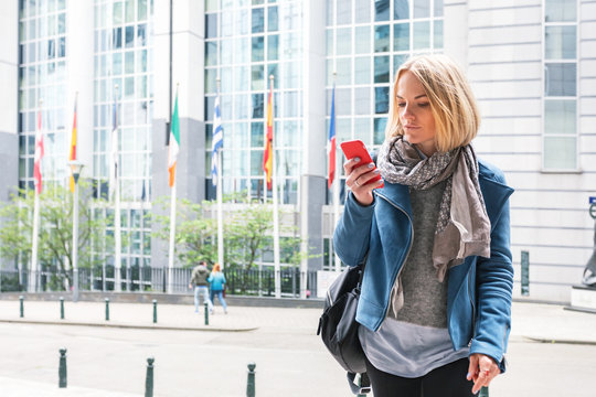 A young woman stands with a telephone in her hands opposite the European Parliament building in Brussels, Belgium. - Powered by Adobe