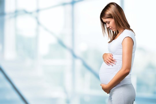 Pregnant young woman in white t shirt on bright background