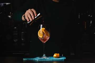 The barman pours Aperol into the cocktail of Aperol Spritz, dark background