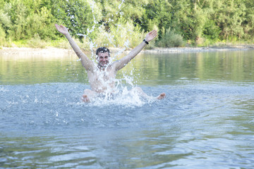 active young happy man makes a splash in the water of a clear mountain river or lake