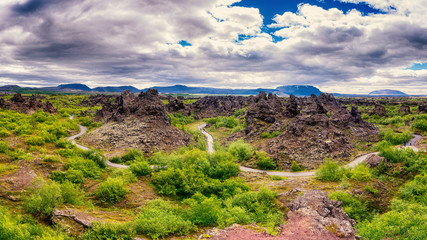 Dimmuborgir lava fields near Myvatn in Iceland. Amazing nature landscape, panoramic view of popular tourist attraction - green valley, rock formations and blue cloudy sky, outdoor travel background
