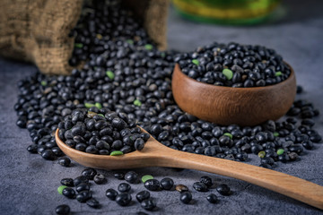 Sack of black beans spill beans with black beans in a wooden spoon on dark table.