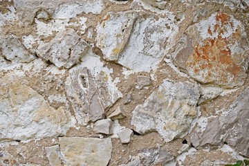 The texture of the stone wall.Outdoors view of an old high stone wall. Weathered surface with imperfections. Blocks pattern of different sizes and shapes. Damaged structure.