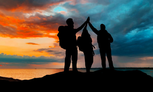 travel, tourism and hike concept - group of travelers with backpacks making high five over sunset background