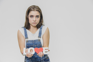 Horizontal portrait of pretty woman with puzled expression, finds solution, wears casual t shirt with denim overalls, isolated over white background. Adorable lovely female student thinks indoor