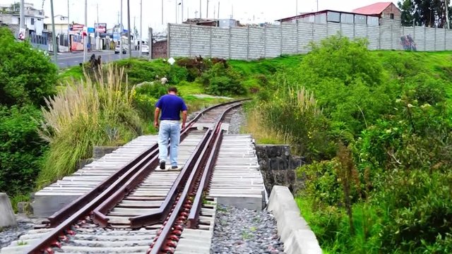 A man walking along a railway while crossing over a bridge.