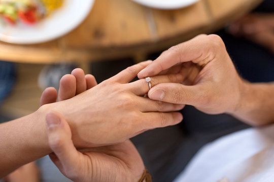 proposal, engagement and relationships concept - close up of man putting diamond ring to female hand at restaurant