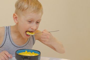 A boy in a gray T-shirt has a breakfast of cornflakes with milk.