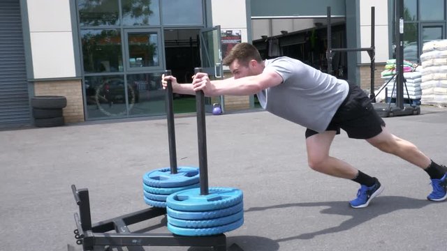 Man Pushing Weighted Sled Through Parking Lot