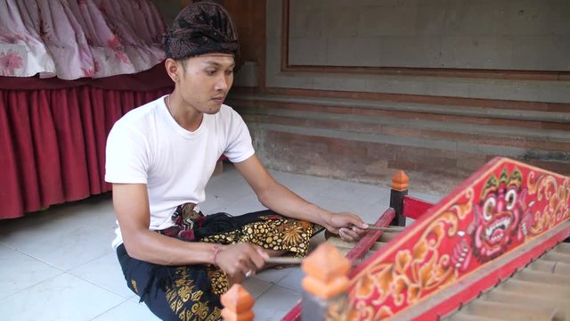 Man in Bali playing music on a colorfully decorated tingklik, bamboo xylophone, at the local temple. Brightly painted percussion instrument being played by young man in Indonesia. Camera orbiting.