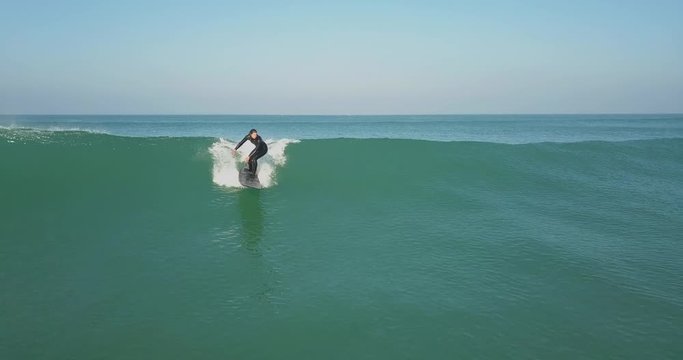Girl on a longboard surfing as the drone flying with her on the wave on a very sunny day in cold water surf with an aerial view