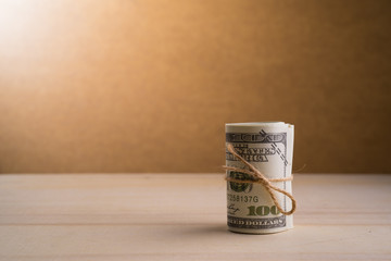 A roll of American currency (USD, American dollars) with 100 dollars bank notes on the outside as a symbol of plenty of money on the wooden background. 