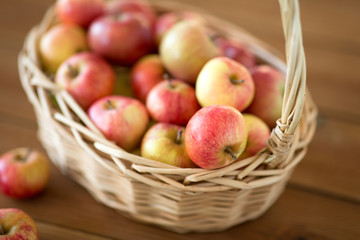fruits, food and harvest concept - ripe apples in wicker basket on wooden table