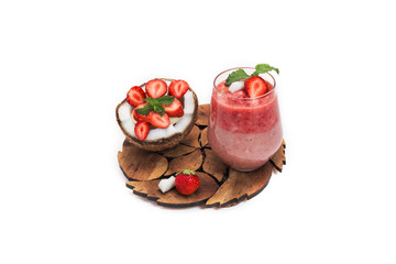 cut coconut with banana and strawberry slices with mint on a wooden carved stand and strawberry two-layer cocktail in a glass with a piece of strawberry and coconut