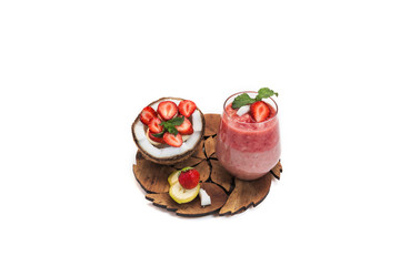cut coconut with banana and strawberry slices with mint on a wooden carved stand and strawberry two-layer cocktail in a glass with a piece of strawberry and coconut
