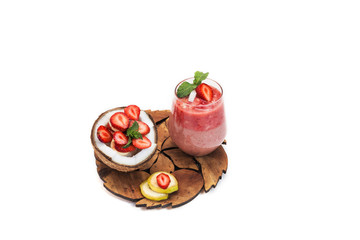 cut coconut with banana and strawberry slices with mint on a wooden carved stand and strawberry two-layer cocktail in a glass with a piece of strawberry and coconut