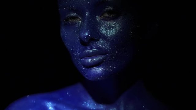 Portrait of beautiful woman with blue sparkles on her face. Girl with art make-up in color Light. Fashion model with colorful makeup