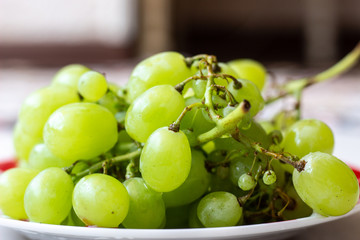 Ripe green grapes in plate on white wooden table, top view. Green grapes in a plate on the table. Green grapes in a red plate on the table.