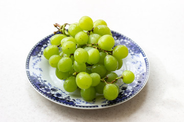 Ripe green grapes in plate on white wooden table, top view. Green grapes in a plate on the table. Green grapes in a red plate on the table.