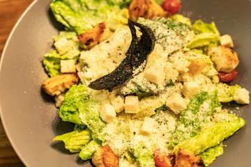 Healthy caesar salad in brown plate on dark wooden table with Shallow depth of focus over dark grunge background
