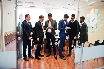 Fototapeta premium Six multiracial business mans standing at office and use mobile phones. Diverse group of male employees in formal wear with cellphones.