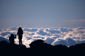 sunset silhouette of two women top of mountain above clouds