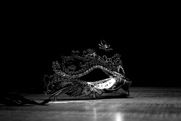 Mask of mystery. A black and white portrait of a venetian mask on a wooden table surrounded by...