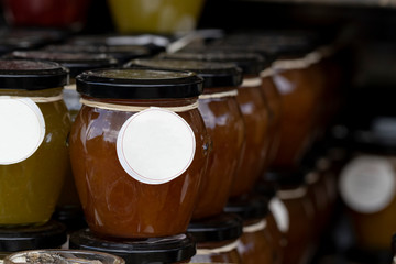 A close up portrait of a row of stacked glass pots with a metal black lid on top, and a label around them. They contain jam or jelly in a fruit or mixed fruit flavour.