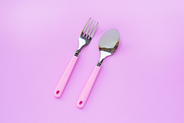 Fork and spoon on pink background.