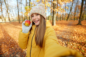 season and people concept - happy girl with apple taking selfie at autumn park