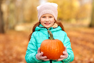 childhood, season and people concept - happy redhead girl with pumpkin at autumn park