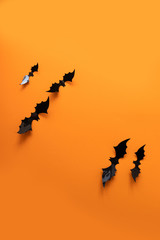 Creative top view halloween composition of black paper bats fly up on an orange background