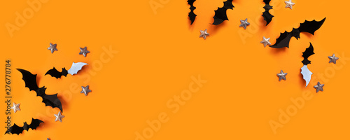 Halloween flat lay composition of black paper bats fly up and gold stars on an orange background