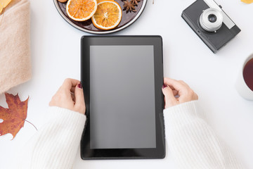 technology and season concept - woman's hands with tablet computer, film camera, autumn leaves and dried orange slices on white background