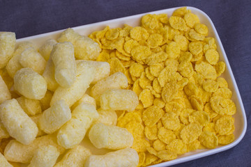 Corn sticks and cornflakes in white plate, top view.