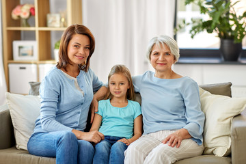 Obraz premium family, generation and female concept - portrait of smiling mother, daughter and grandmother sitting on sofa at home