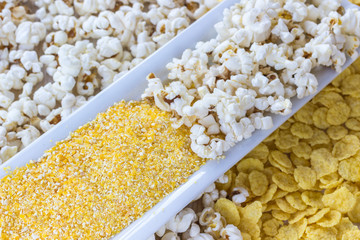 Obraz premium Cornmeal, cornflakes and popcorn in white plates, top view.
