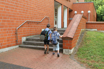 two junior schoolchildren with backpacks go to school, rise, holding hands, on the porch of the...