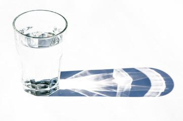 Water glass with strong shadows on white background
