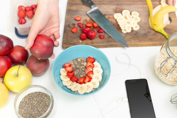 Woman preparing healthy fitness breakfast: oatmeal with bananas, strawberries and chia seeds