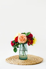 Stunning composition of colorful roses in a glass vase on a wicker napkin