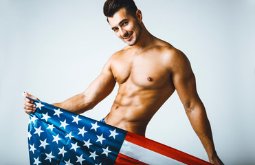 Portrait of shirtless handsome young man with stylish haircut posing with American flag over gray background. Perfect hair & skin. Close up. Studio shot