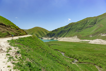 Fototapeta na wymiar Tourists go on the road to lake Kezenoi Am in Botlikh district of the Republic of Dagestan. Below the river flows to Kharsum. Sunny day