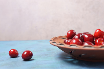 Red sweet cherry in a clay plate on a turquoise table
