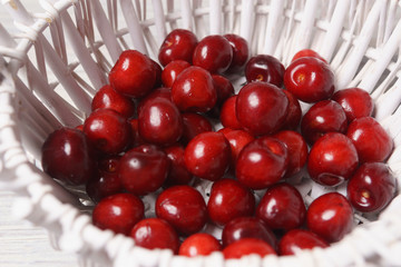 Red sweet cherries in a white basket on a white wooden table