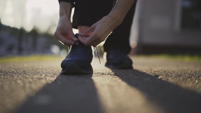 Woman runner tying laces of running shoes for jogging at sunset