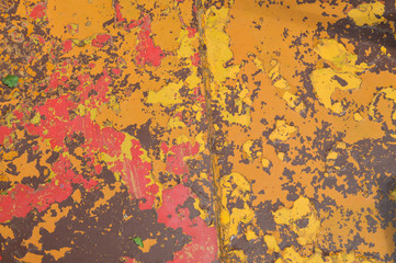 Texture of iron metal painted multicolored red yellow peeling paint of old battered scratched cracked ancient rusty metal sheet wall with corrosion. The background